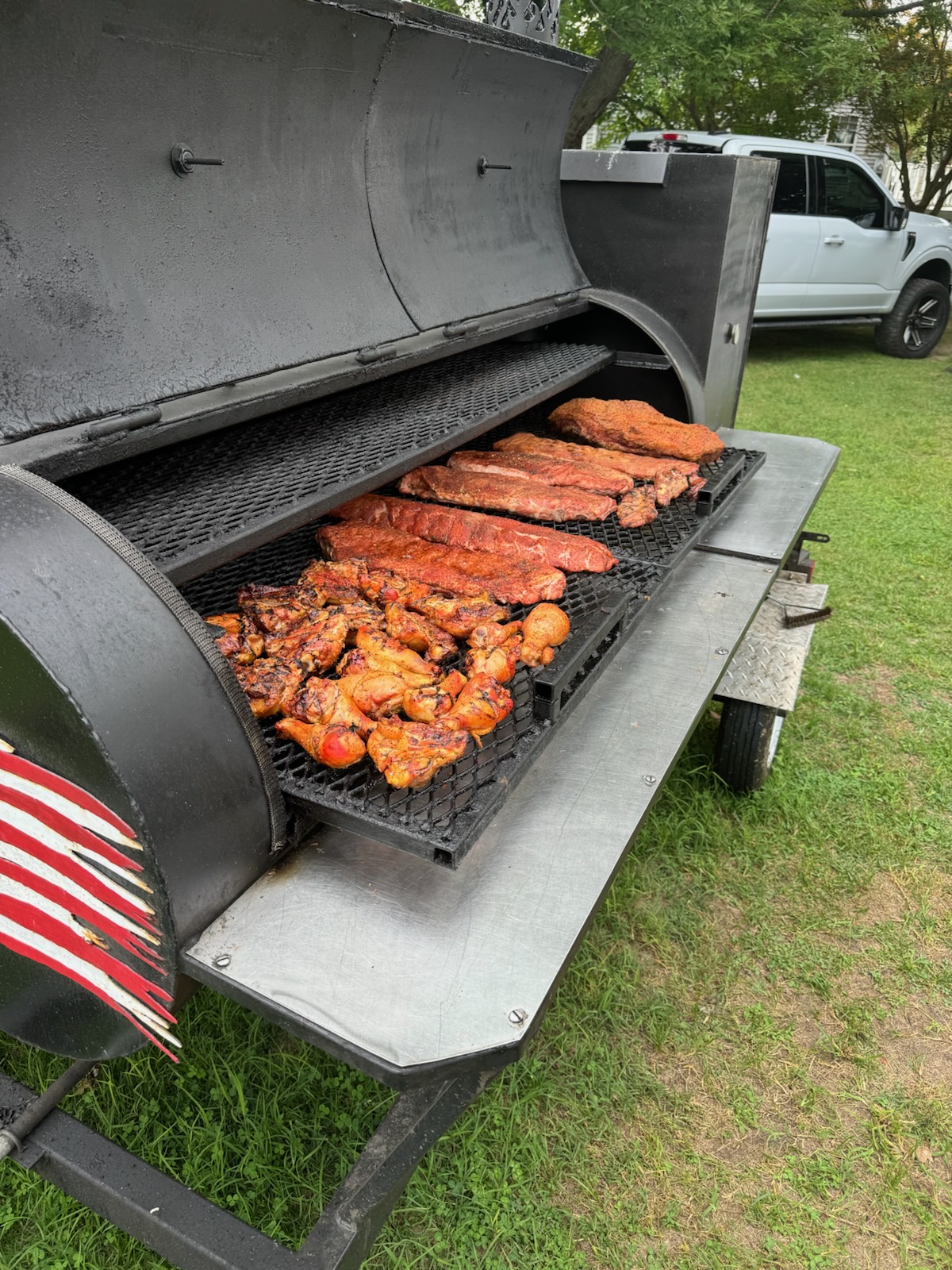 Offset trailer smoker loaded with ribs and chicken, American flag firebox